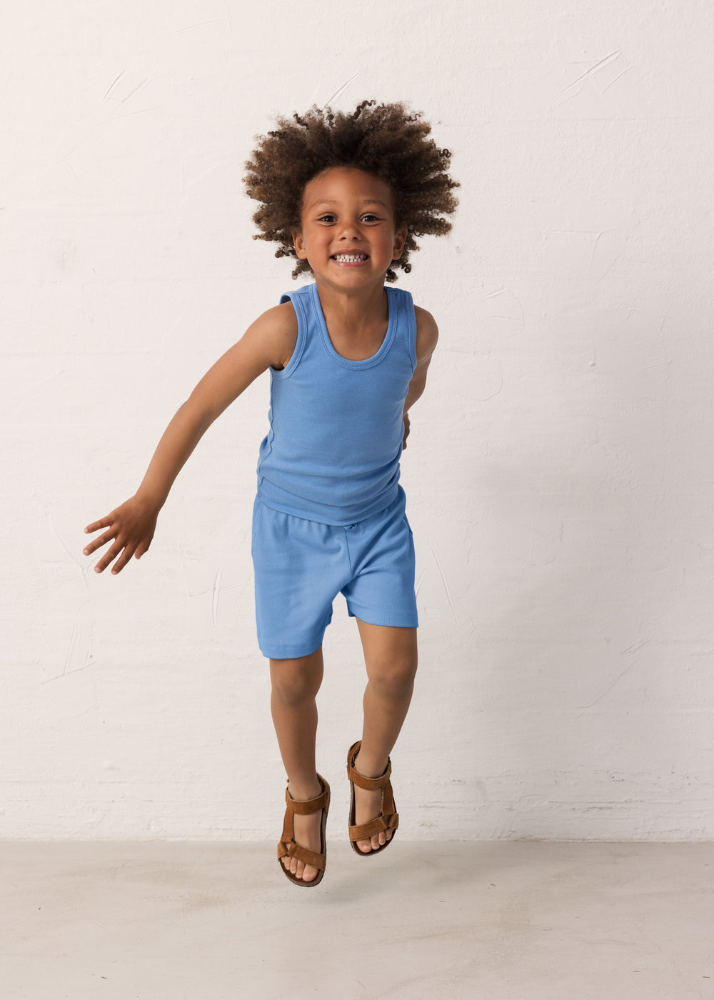 Dreng der hopper i blå shorts og matchende undertrøje