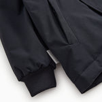 Dark jacket sleeve with ribbing and pocket seam, dark front detail.
