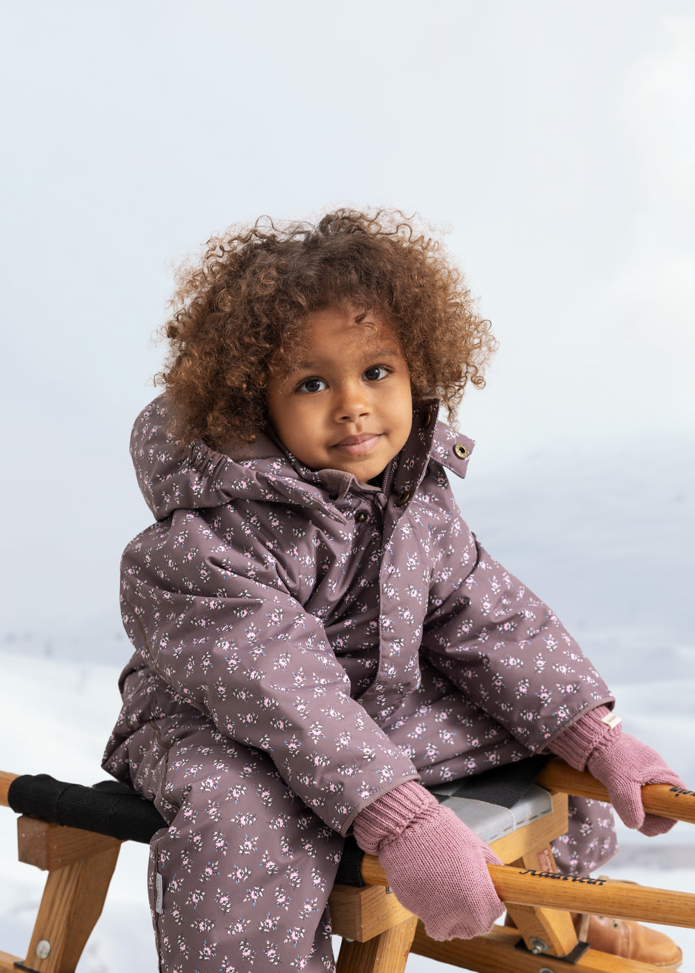 Baby in dusty pink gloves with ribbed cuffs on the hands.
