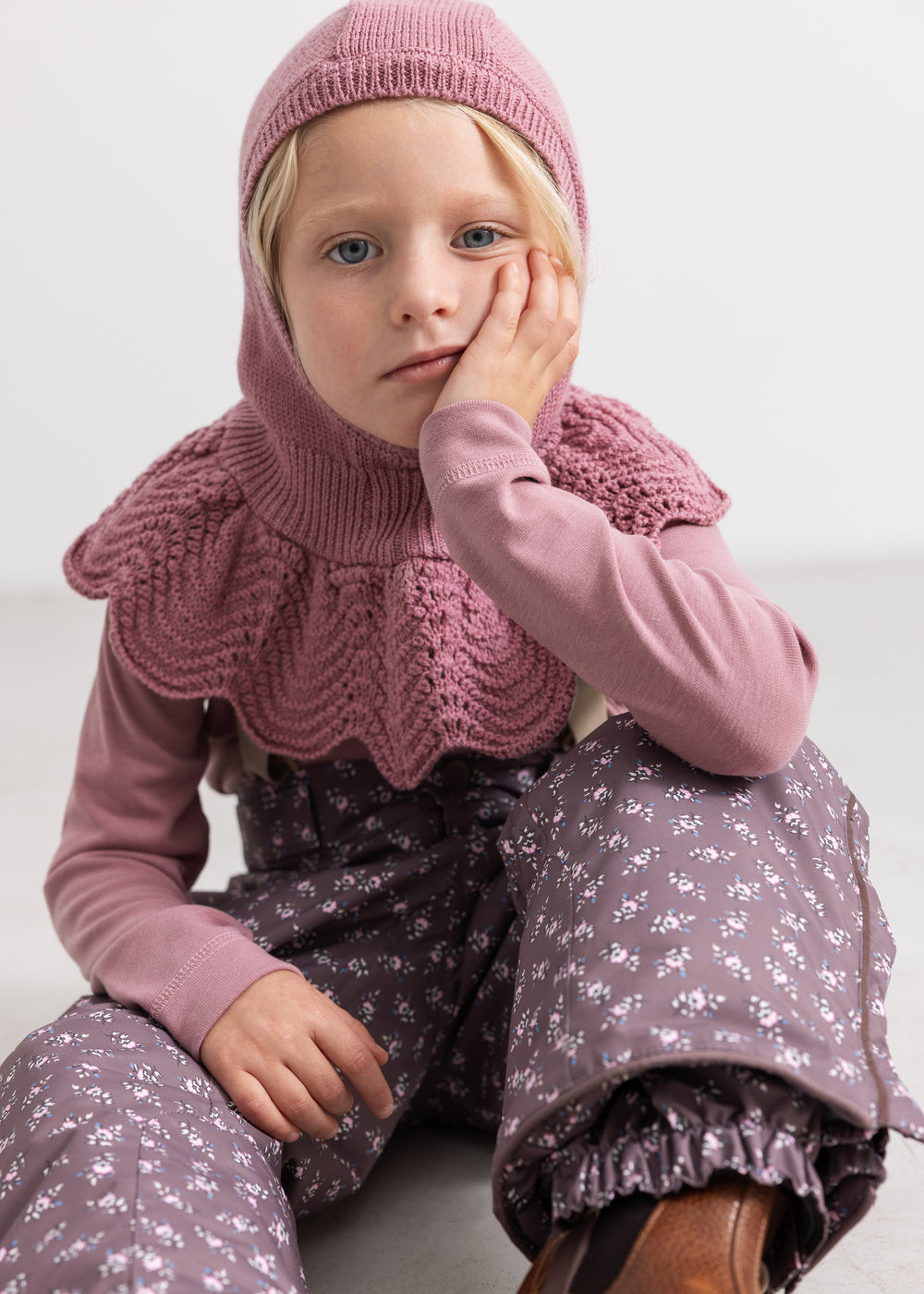 Child wearing a rose‑brown knitted hat with ribbed edge and crinkled bacon edge.