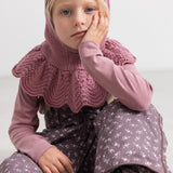 Child wearing a rose‑brown knitted hat with ribbed edge and crinkled bacon edge.