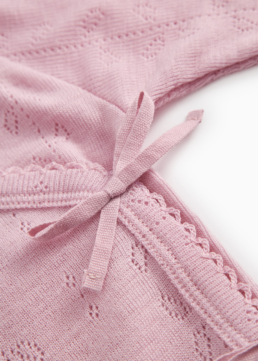 Pink baby jumpsuit with a bow at the chest and a finely dotted embroidery structure.