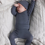 Baby in a white onesie with a dark gray ribbed hat and matching leggings.