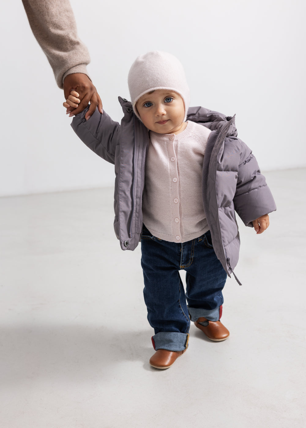 Pink baby cardigan with button closure, visible under a gray winter jacket.