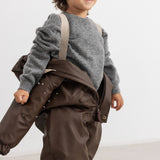 The PU jacket in dark brown with hood and large pockets, seen from the side.