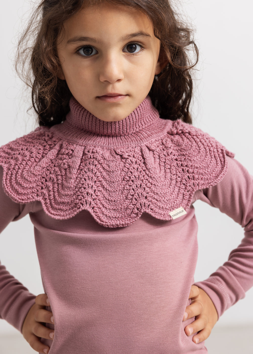 Knitted turtleneck in muted rose color worn over a long-sleeve shirt