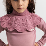 Knitted turtleneck in muted rose color worn over a long-sleeve shirt