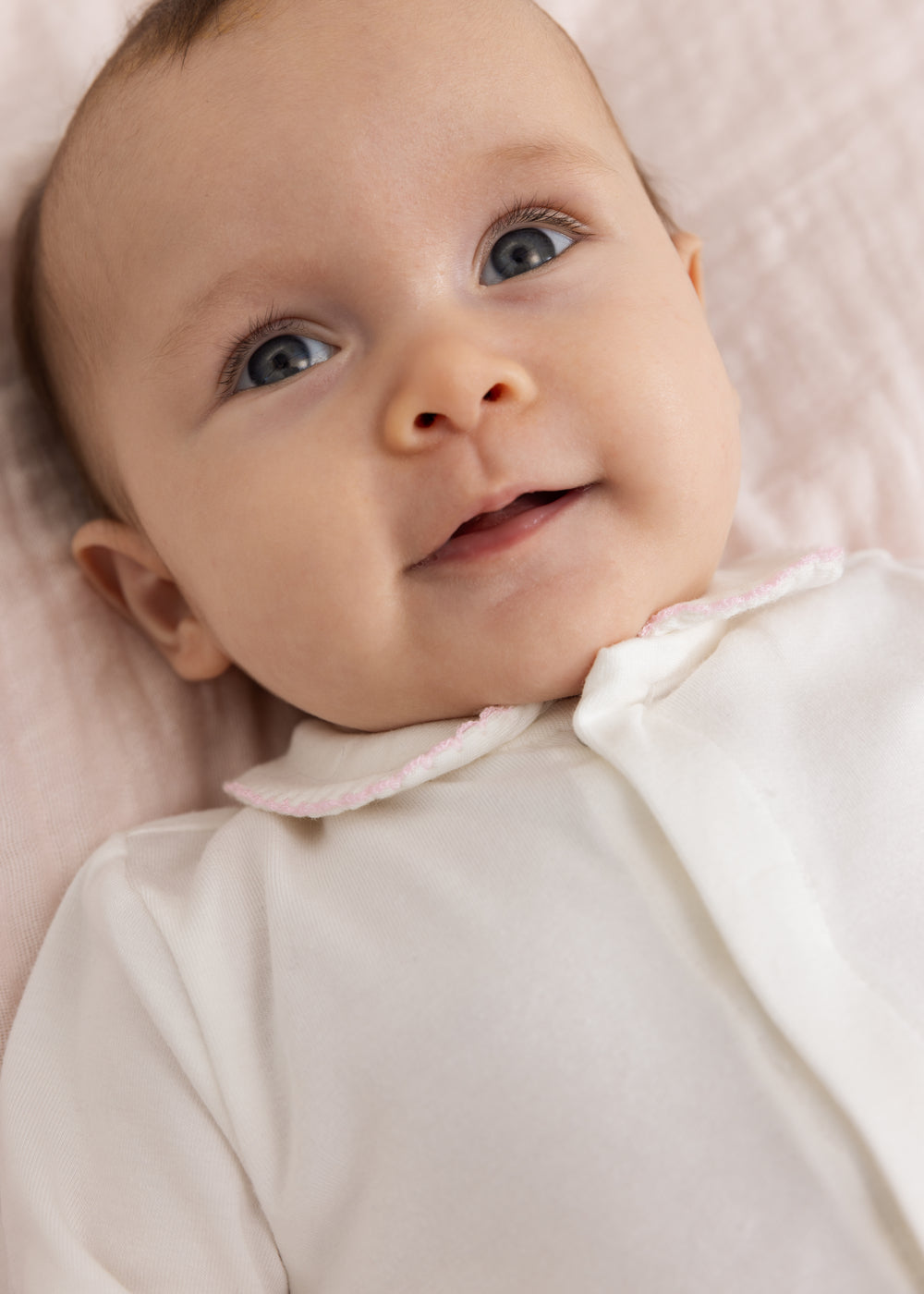 Baby off-white jumpsuit with pink collar and button detail.