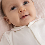 Baby off-white jumpsuit with pink collar and button detail.