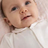 Baby off-white jumpsuit with pink collar and button detail.