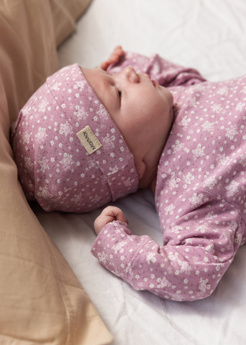 Baby wearing a pink hat with small white flowers and a matching jumpsuit.