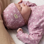 Baby wearing a pink hat with small white flowers and a matching jumpsuit.