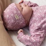 Baby wearing a pink hat with small white flowers and a matching jumpsuit.