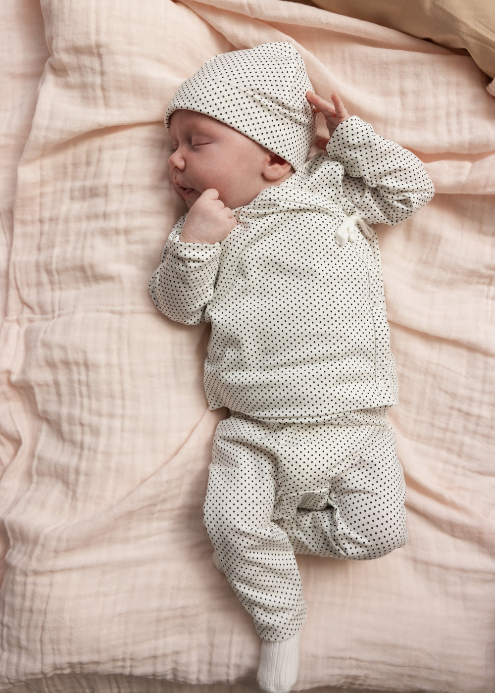 A gray patterned baby set with a hat and long legs, baby lying on the bedding.