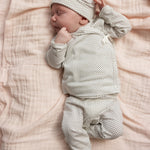 A gray patterned baby set with a hat and long legs, baby lying on the bedding.