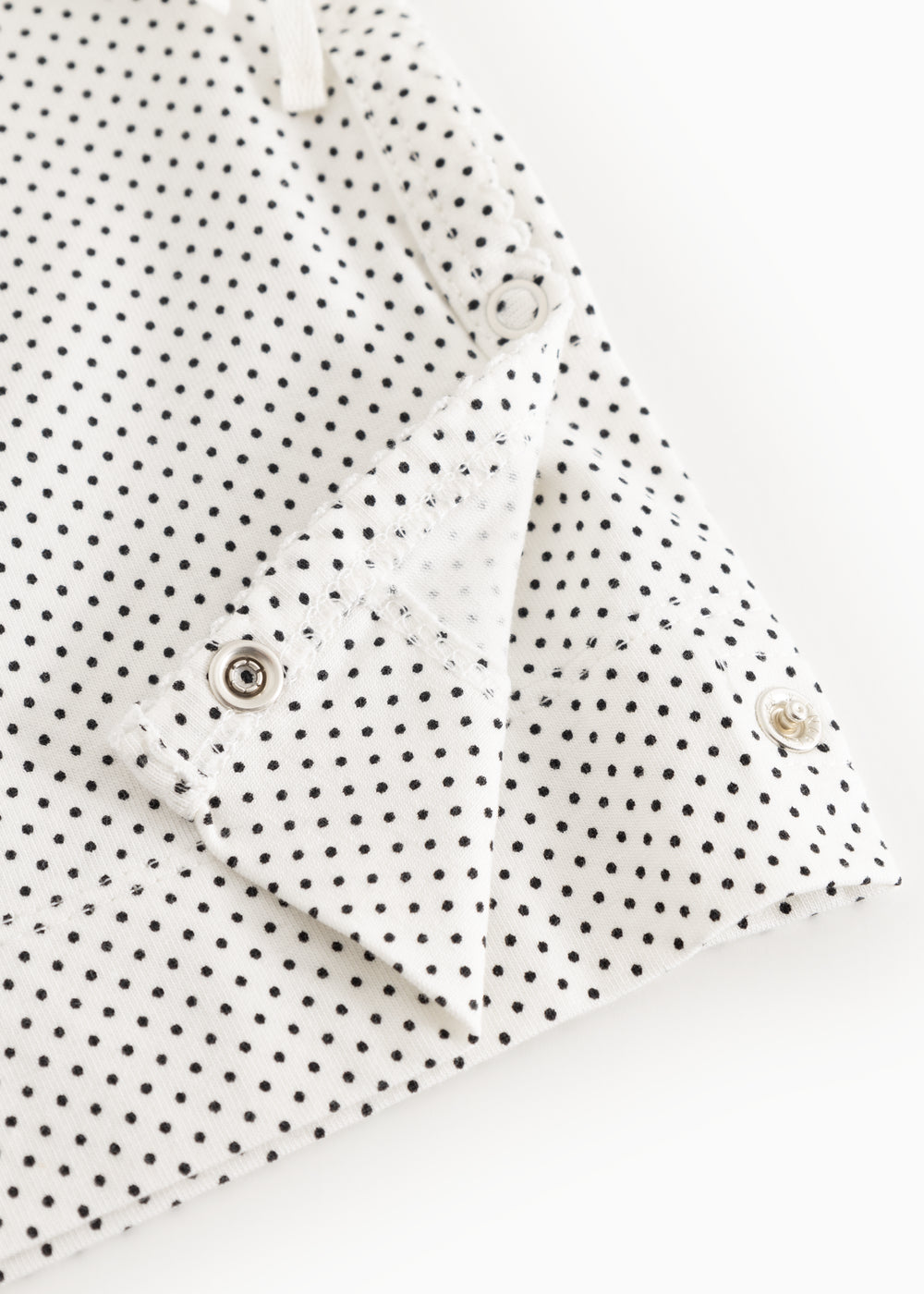 White baby top with small black dots and snap closure at the shoulder