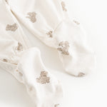 White dress with beige teddy bear print and long legs, shown as a close-up at the feet.