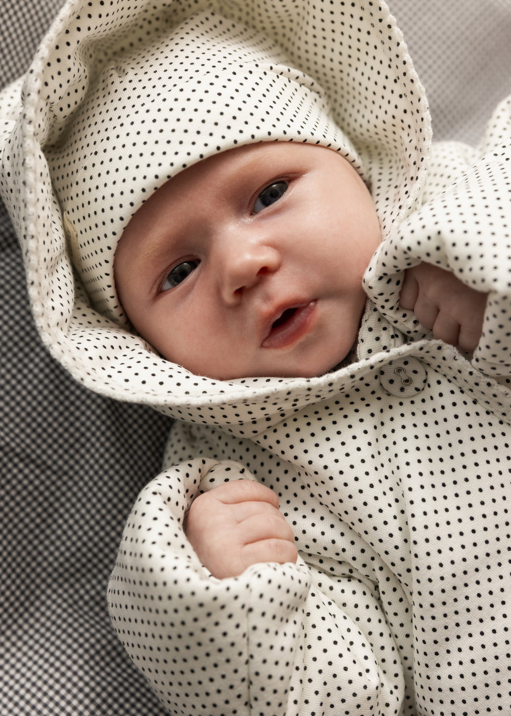 Baby in white knitted jacket with small black dots and button closure.
