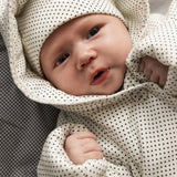 Baby in white knitted jacket with small black dots and button closure.