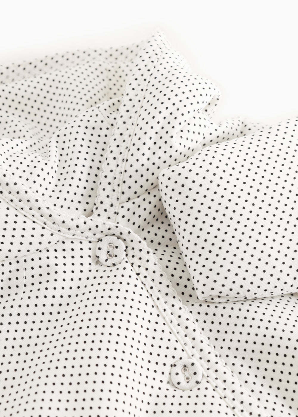 Details of a white jacket with small black dots, hood, and buttons at the front.