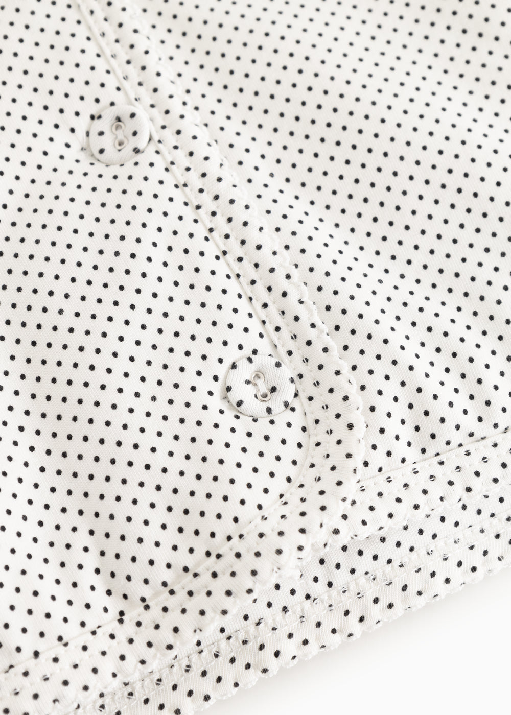 White children's jacket with small black dots and snap closure in front.