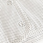 White children's jacket with small black dots and snap closure in front.