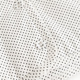 White children's jacket with small black dots and snap closure in front.