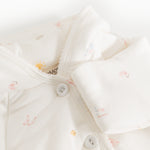 Hooded cream jacket with front button closure and wavy edge at the hood.