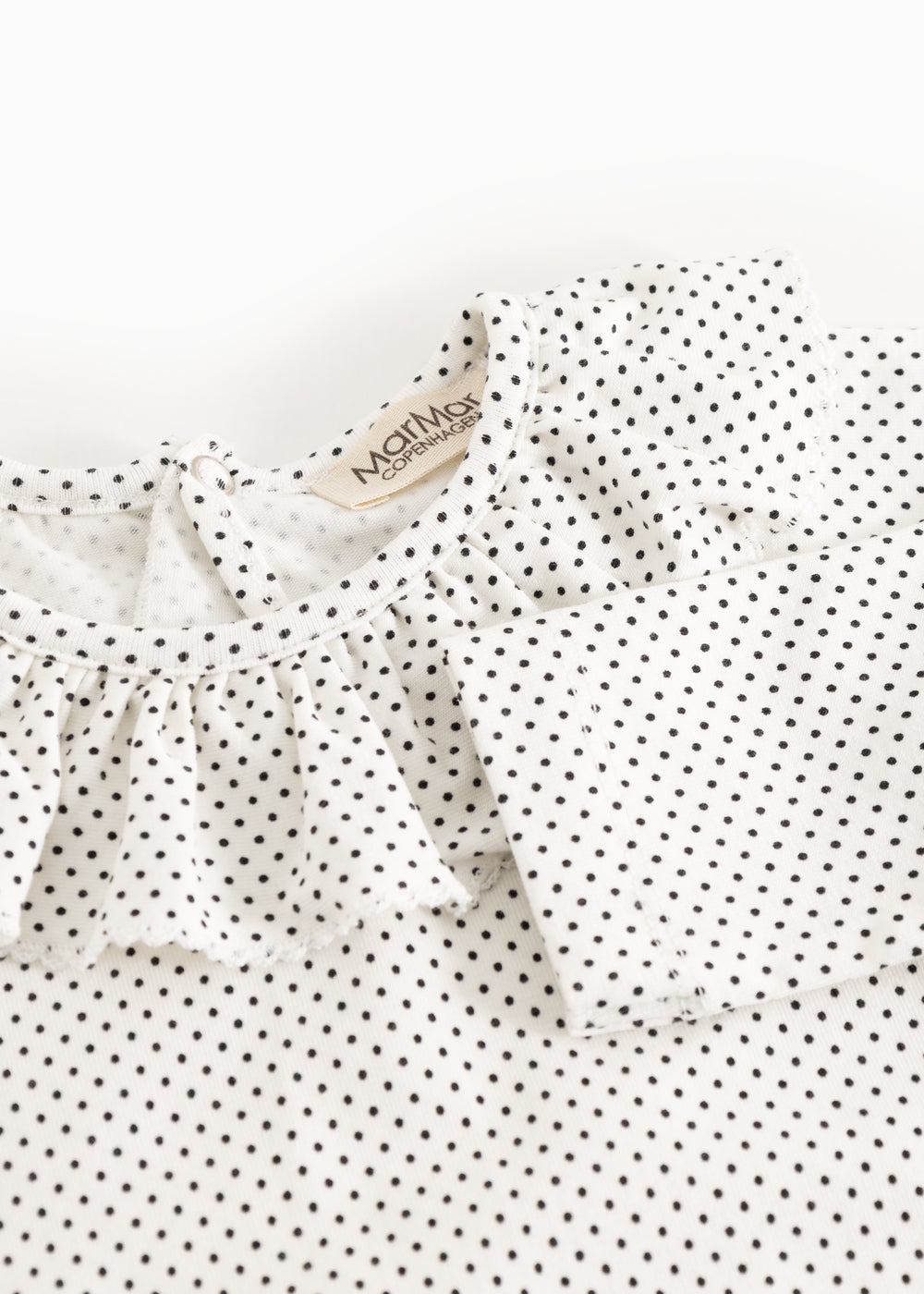 Details of baby bodystocking with small black dots and a bacon edge at the neckline.