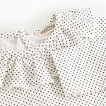 Details of baby bodystocking with small black dots and a bacon edge at the neckline.