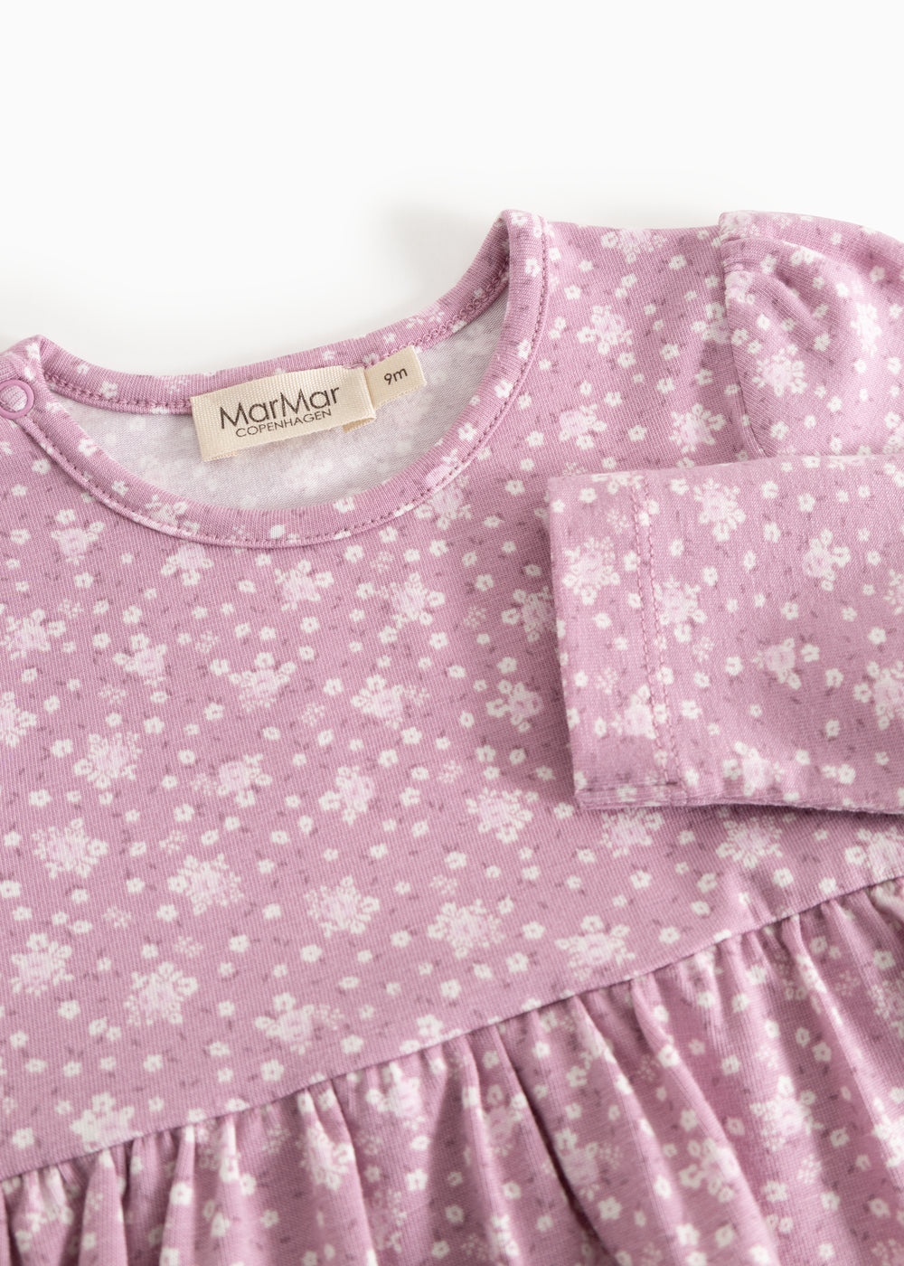 Details of a pink dress with floral print, round neckline, and pleated bust.
