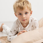 Kids pajamas in off‑white with teddy bear print, shown on children.
