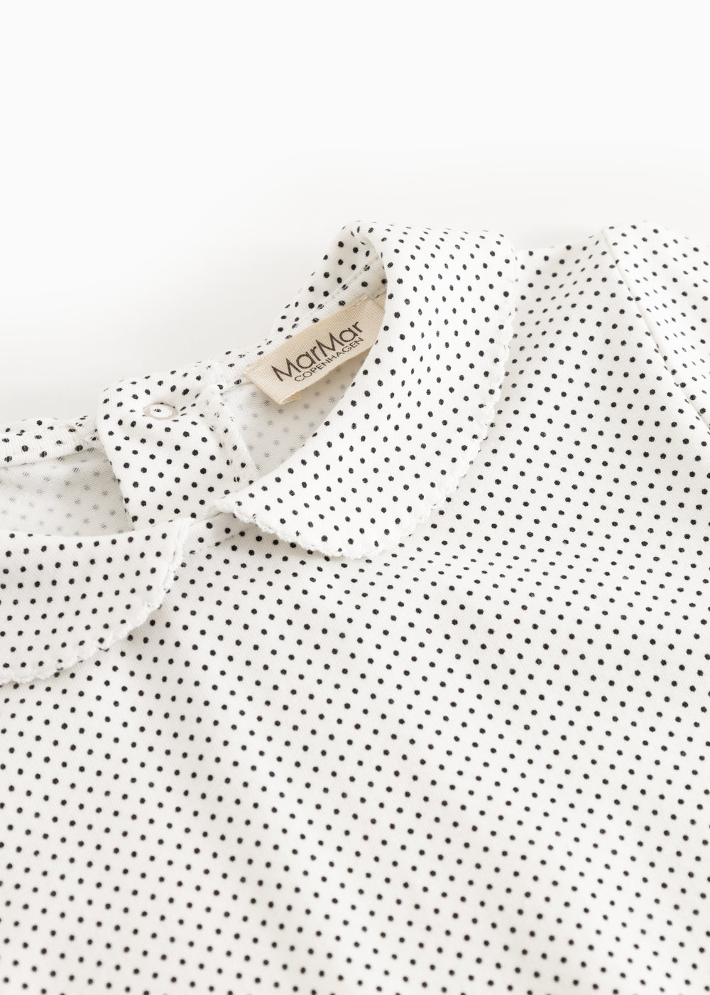 White long-sleeve t‑shirt with small black dots, collar edge and brand tag at the neck.