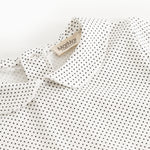 White long-sleeve t‑shirt with small black dots, collar edge and brand tag at the neck.