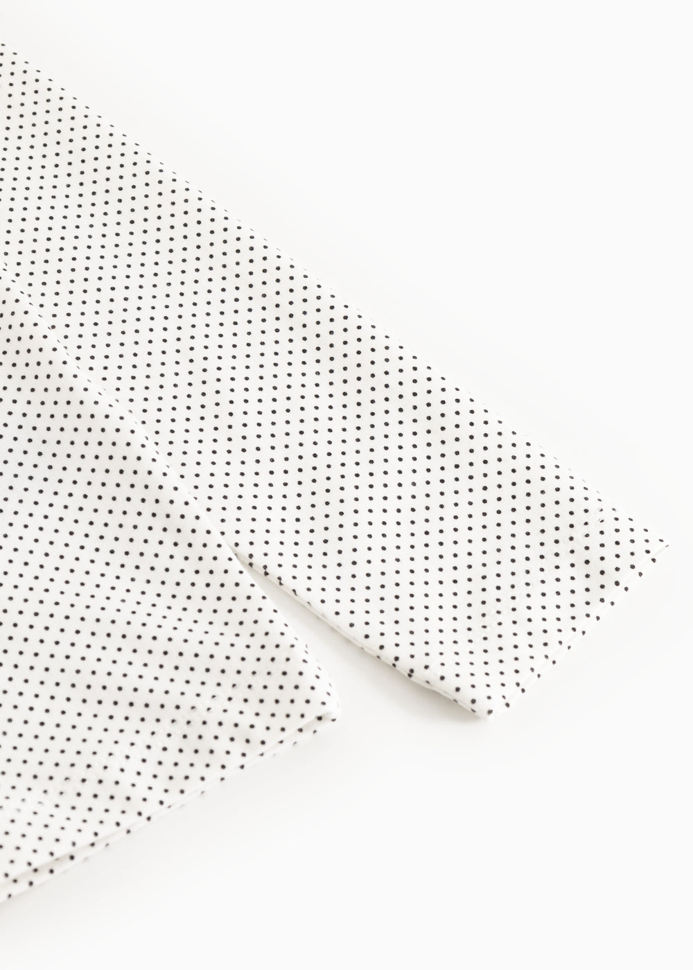 Long-sleeve white T-shirt with small black dots, close-up of sleeve and seam.