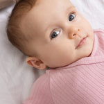 Pink baby jumpsuit with ribbed fabric and round neckline.