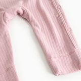 Pink jumpsuit in ribbed texture, long sleeves and leg opening with snap strap.
