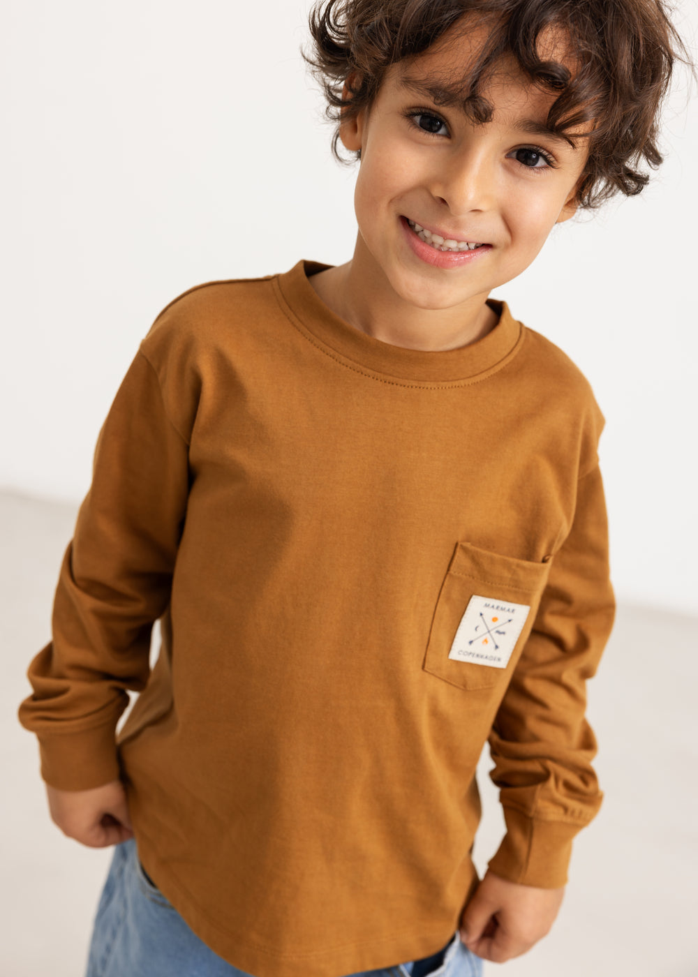 Caramel brown long-sleeve blouse with chest pocket and round neckline, worn by a child.