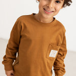 Caramel brown long-sleeve blouse with chest pocket and round neckline, worn by a child.
