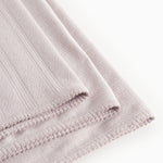 Light lilac rug in woven pattern with fringe edge and stitching along the edge.