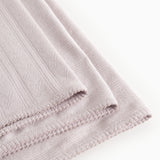 Light lilac rug in woven pattern with fringe edge and stitching along the edge.