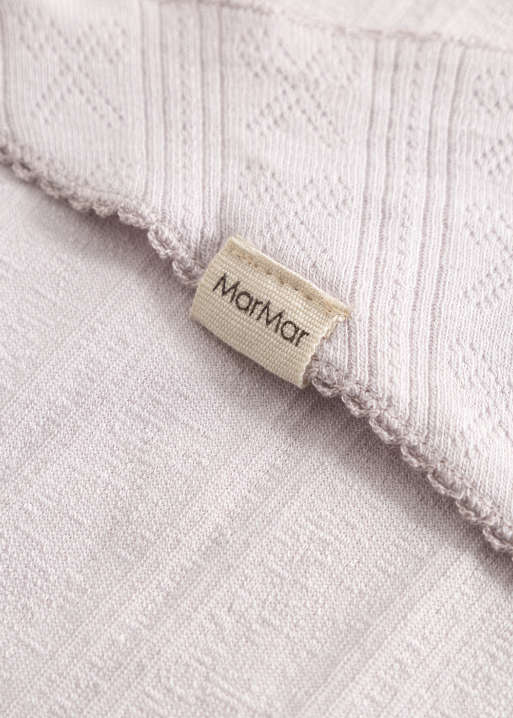 Light pink scarf with fringe edge and woven pattern, detail with brand.