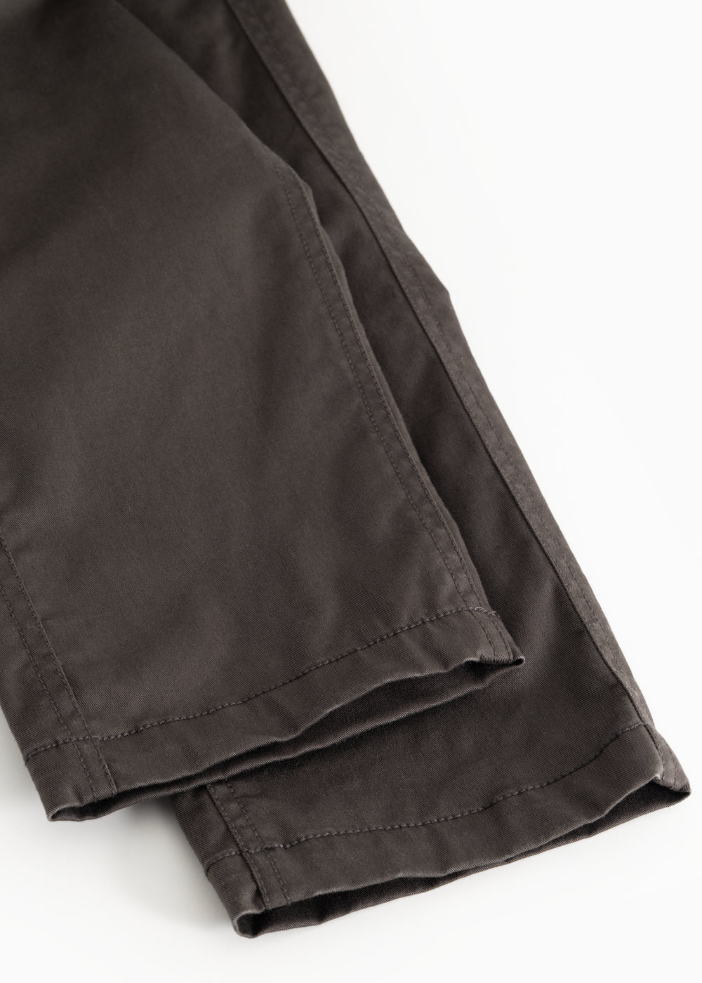 Dark pants with slanted seam and cuff at the leg opening.