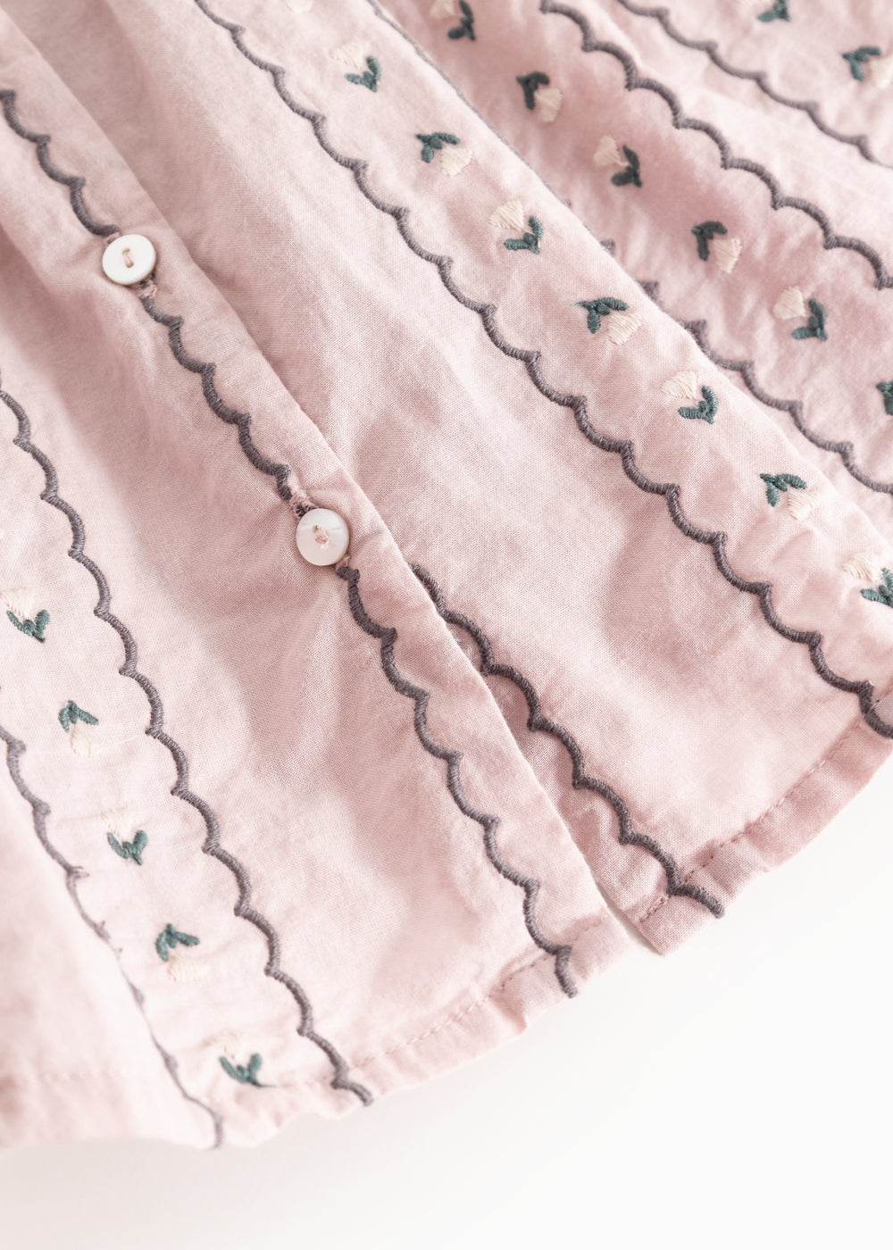 Pink blouse with button closure and wavy edges featuring small embroidered flowers.
