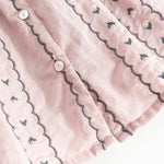 Pink blouse with button closure and wavy edges featuring small embroidered flowers.