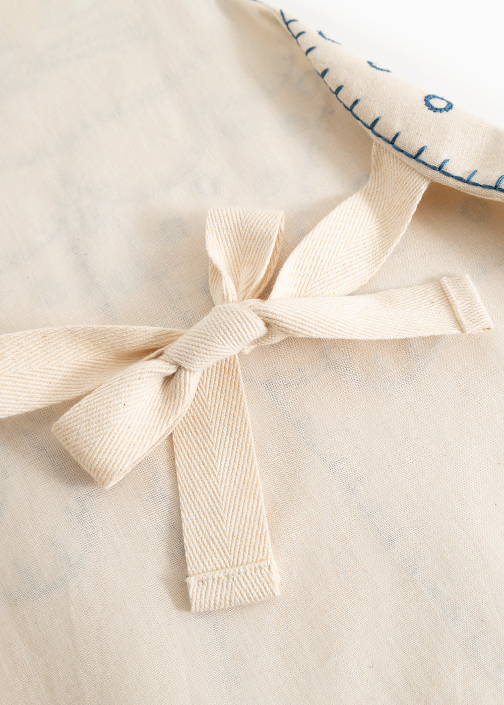 Natural-colored apron with tie strap and fabric bow in front, visible textures