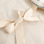 Natural-colored apron with tie strap and fabric bow in front, visible textures