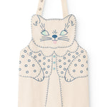 Natural-colored apron with cat appliqué, blue embroidery, and shoulder button closure.