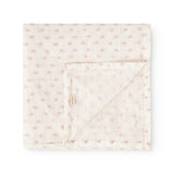 Baby swaddle folded and fastened with a strap, cream-colored with small pink flowers.