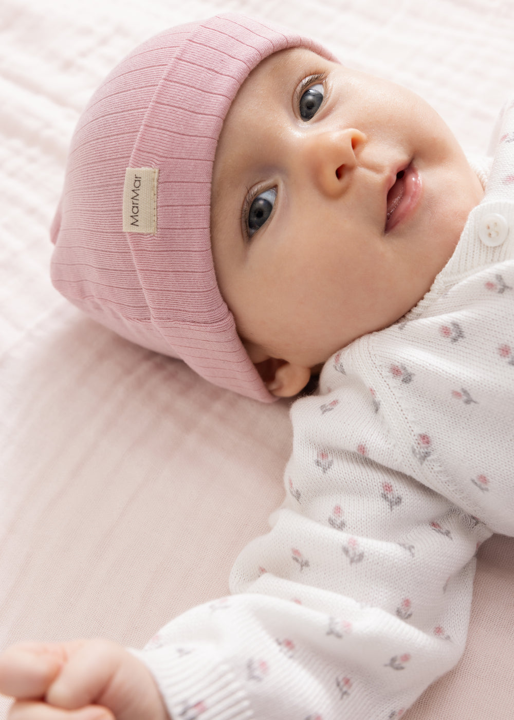 Pink baby hat on baby with white jumpsuit with small patterns